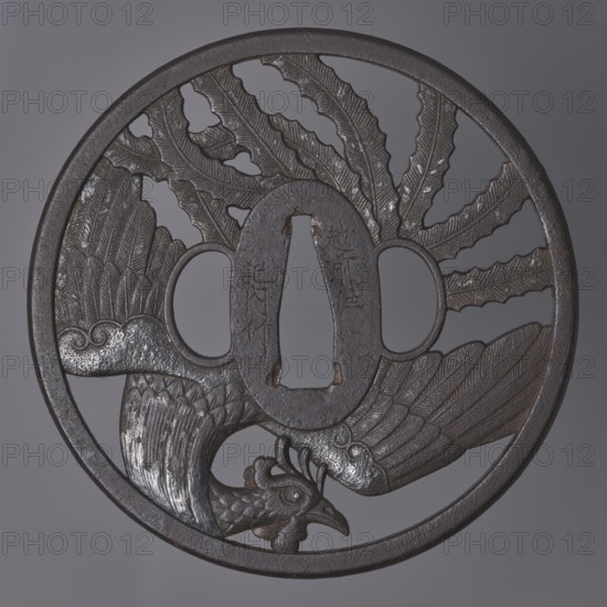 Crossguard tsuba, Kinai,  school, Echizen Kinai,  school; phoenixes iconography, hoo phoenix; sword crossguard for katana; Japanese art/culture; weapon, melee weapon; Edo 1603–1868 swords. Tsuba: round maru-gata with a rectangular edge with slight convexity kaku mimi ko-niku; oval seppa-dai; oval ryôhitsu ana matching usual kozuka hitsu ana. Decoration: mythical bird hôô with spread wings and long tail feathers arranged in a fan-like pattern, incorporated into a circle on both sides; plumage details engraved. ca. 1800 Edo Period, 1603–1868, Japan. Diameter 9.3 cm; thickness 0.5 cm., A circular metal object with a dark brown to black patina features an openwork design of a bird with detailed feathers and a curved beak, occupying the lower half, and a pattern of large stylized feather shapes radiating from the center to the upper edge; the surface shows areas of worn lighter gray where the metal is polished or abraded, and the rim is smooth and slightly raised.