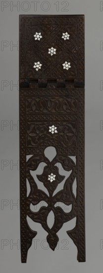 Quran lectern rahla, Islamic art, Turkish, Ottoman dynasty 1299–1922; Quran lectern decorated with arabesques, geometric ornament, rosettes, lotus/tulip motif; 19th century, Turkey; piece of furniture; unfolded: height 50.6 cm, width 91.5 cm, depth 21.3 cm, weight 1.7 kg; folded: height 80.5 cm, width 21.3 cm, weight 1.7 kg., A tall, narrow carved wooden panel with a dark brown surface featuring intricate floral and geometric relief patterns and openwork sections; several small white star-shaped inlays are set within the carved designs, creating contrast against the dark wood; the panel shows a hinged top section with carved borders and repeating motifs, and the lower portion includes flowing vine-like openwork and pointed feet; the overall colors visible are dark brown wood, white inlays, and a neutral gray background.