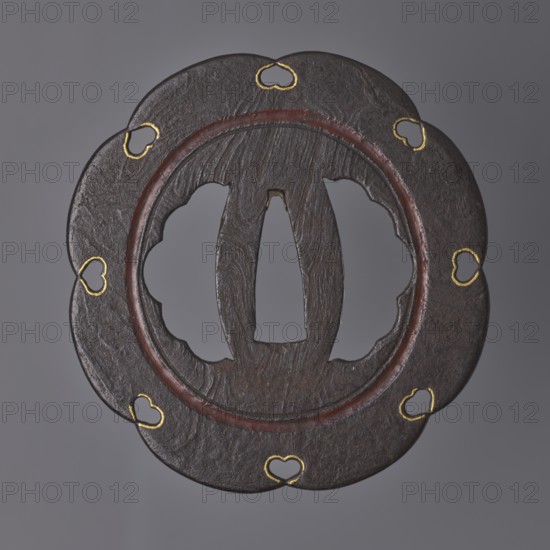 Crossguard tsuba, Kasuga school; maker: Kunihide. Tsuba in the shape of an eight-petaled flower hachi mokkô; both hitsu cut into an identical multi-petaled shape. The central part is enclosed by a fairly wide, recessed circle stained with dark red lacquer, with openwork heart-shaped cutouts inome type at the edge between the petals, emphasized by delicate gold inlay. The surface of the guard is partly of the mokume tetsu type imitation of wood grain. 17th century Edo period, 1603–1868. Japan, Higo province. Tsuba; diameter 8 cm, thickness 0.25 cm., A round, scalloped metal object with a central open area and carved interior shapes sits against a neutral gray background; the metal surface is dark brown to near-black with visible textured grain and a slightly reddish-brown inner ring, and there are a few small heart-shaped cutouts around the outer edge highlighted with a bright gold color.