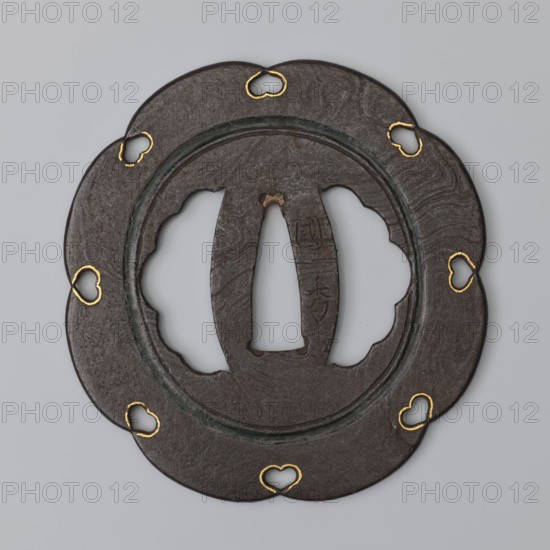 Crossguard tsuba, Kasuga; maker: Kunihide; Japanese; Edo period 17th century, 1603–1868; Higo province. Tsuba in the shape of an eight-petaled flower hachi mokkô; both hitsu cut into an identical multi-petaled shape. Central part enclosed by a fairly wide recessed circle stained with dark red lacquer, with openwork heart-shaped cutouts inome type at the edge between the petals, emphasized by delicate gold inlay. Surface partly of the mokume tetsu type imitation of wood grain. Function: sword crossguard katana tsuba. Diameter 8 cm; thickness 0.25 cm., A round, scalloped metal object with a central opening and a raised inner ring, shown against a light gray background; the metal surface is dark brown to almost black with a textured, slightly mottled appearance, and several heart-shaped cutouts around the edge are highlighted with gold-colored inlay; the inner area has irregular cut openings and a vertical central slot, and there are subtle variations of darker greenish patina along the r...