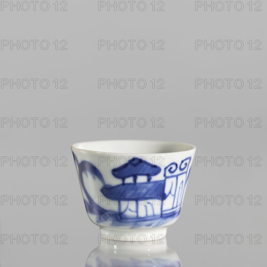 Bowl, ceramics, blue and white porcelain, Qing 1644–1911 style, Chinese, landscapes with architecture and staffage, landscape motifs; porcelain; grayish-white. Bowl with flared edges on a low ring foot, 19th century China; vessel. Height 4.4 cm, diameter 5.8 cm., A small porcelain cup with a white base color and blue painted decoration sits on a reflective surface; the cup has a flared rim and a short foot, and the blue decoration includes stylized architectural shapes and flowing curved lines, with visible shades of blue ranging from deep cobalt to lighter blue tones against the white porcelain.