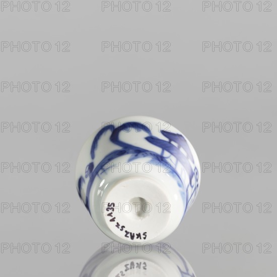 Bowl, ceramics, blue-and-white porcelain, Qing 1644–1911, China, 19th century. Porcelain vessel with flared edges on a low ring foot; height 4.4 cm, diameter 5.8 cm. Decoration: landscapes with architecture and staffage; grayish-white.,  noted., A small rounded ceramic object with a glossy white surface and blue painted brushstroke designs, shown from an end-on angle against a light gray background, with a smooth rounded rim and a recessed central hole, and a faint reflection visible on the surface beneath it.