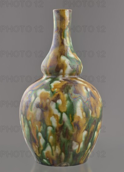 Gourd-shaped vase, from Ignacy Jan Paderewski 1860–1941; Chinese, Qing dynasty 1644–1911, 18th century; vessel; height 19.1 cm, diameter 10.8 cm, weight 0.4 kg., A ceramic vase with a double-gourd silhouette sits against a neutral gray background, its glossy surface showing a marbled, drip-like pattern in shades of green, brown, yellow, white, and iridescent purple-blue. The neck is elongated and tapers to a narrow opening, while the body rounds into a bulbous lower section; the glaze forms flowing, organic patches and streaks that blend and overlap, with some areas appearing more translucent and others more opaque. The base shows a small unglazed spot and the overall finish reflects light, emphasizing the smooth, glazed texture and the multicolored, variegated pattern.