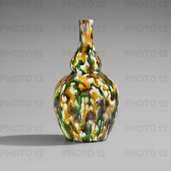 Gourd-shaped vase, Chinese art, Chinese culture, Qing 1644–1911, Qing style, 18th century, China, vessel; height 19.1 cm, diameter 10.8 cm, weight 0.4 kg, A double-gourd ceramic vase with a glossy, mottled surface sits against a plain gray background, displaying a pattern of green, amber-yellow, white, and brown colors that blend and drip together across its bulbous lower body and narrower upper neck, with soft highlights on the glaze and a faint shadow cast to the side.