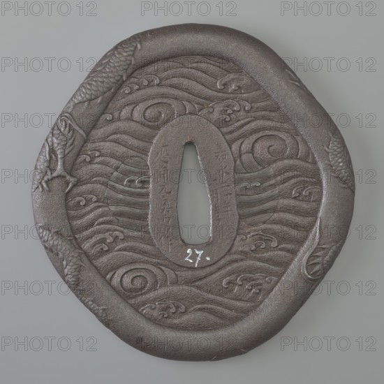 Crossguard tsuba, Raiyôken, Yoshimasa; sword crossguard in the shape of an otafuku chubby woman's face. Edo period, Kaei 5 1852, Year of the Rat, Japan. Iron tsuba, height 8.7 cm, width 8.35 cm, depth 0.5 cm. Oval seppa dai; edge thick, clearly defined and rounded hira dote mimi. Decorated in low relief with two dragons; both sides carved in low relief with rough sea waves umiji. The outlines of the side hitsu holes are visible, later plugged different engraving style. Inscription includes the phrase kitsu jitsu happy day. Maker: Raiyôken Yoshimasa. Function: katana tsuba; motifs: dragons, sea waves, Otafuku., An oval dark brown metal object with a central teardrop-shaped opening is shown against a light gray background; the object's surface features carved swirling wave patterns and spiral motifs, with textured raised borders and carved fish-like forms along the edges, and visible shades of dark brown and gray across the metal.