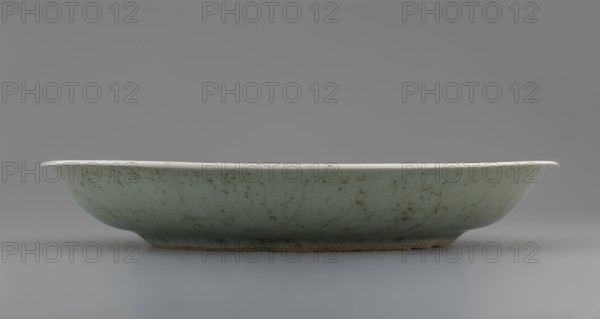 Plate, Chinese, Qing dynasty 1644–1911, 18th century; porcelain vessel with inscriptions and decoration of lotuses and plants; height 3.5 cm, diameter 21.6 cm, weight 0.5 kg., A shallow ceramic dish with a gently flared rim sits on a neutral surface, showing a pale green glaze with darker mottled speckles and crazing lines; the rim appears off-white, the underside near the base shows a warm brown exposed clay, and the background and surface are shades of gray.