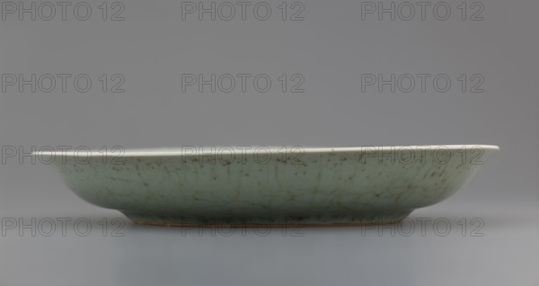 Plate, gift, Chinese art, Chinese, Qing 1644–1911, Qing style, inscriptions, lotuses, plants, 18th century, China, vessel, height 3.5 cm, diameter 21.6 cm, weight 0.5 kg, A shallow, oval ceramic dish sits on a smooth surface, shown in profile with a low foot and gently flared rim; the exterior glaze is a pale greenish-blue with visible crackle patterns and small darker speckles, while the rim appears off-white and the unglazed foot edge shows a brownish clay tone; the background and surface are neutral gray.