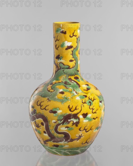 Vase, Qing dynasty Kangxi period, 1662–1722, Chinese, porcelain cylindrical-neck vessel with fa-hua decoration depicting dragons; height 41.0 cm, diameter 24.3 cm, weight 3.0 kg., A tall ceramic vase with a long narrow neck and rounded body sits against a plain light gray background; the vase has a glossy yellow ground decorated with a group of sinuous dragons in shades of green and dark brown, accented by cloud-like motifs in pale green and white, and stylized flame shapes in dark brown, with a band of green wave patterns around the base.