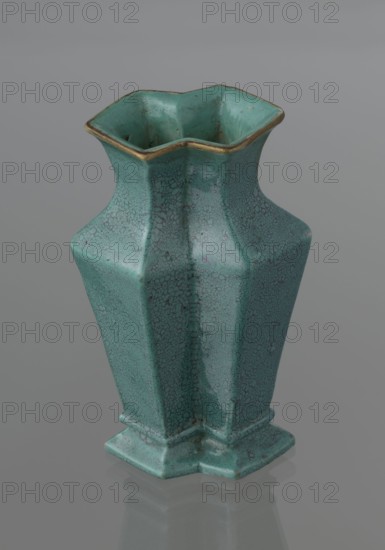 Vase, Qing style, ceramics, Chinese art, Chinese culture, Qing dynasty 1644–1911, 19th century, China, vessel; height 11.6 cm, width 4.7 cm, depth 7.15 cm., A ceramic vase with a textured crackle surface in shades of turquoise and teal, with a slightly darker mottling throughout and a thin metallic gold rim at the flared, scalloped top; the vase has an angular, faceted form that narrows at the neck and widens toward a stepped, hexagonal base, and it sits on a smooth gray reflective surface against a neutral gray background.