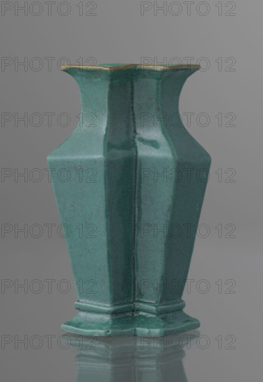 Vase, gift, Chinese, Qing dynasty 1644–1911, ceramics. Covered with a turquoise glaze with manganese spots. 19th century, China. Vessel; height 11.6 cm, width 4.9 cm, depth 7.1 cm, weight 0.15 kg., A teal ceramic vase with a matte crackled finish and a hexagonal, faceted body standing on a matching base, with a flared rim that has a thin gold-colored edge; the vase casts a soft reflection on a glossy surface and is set against a smooth gray background.