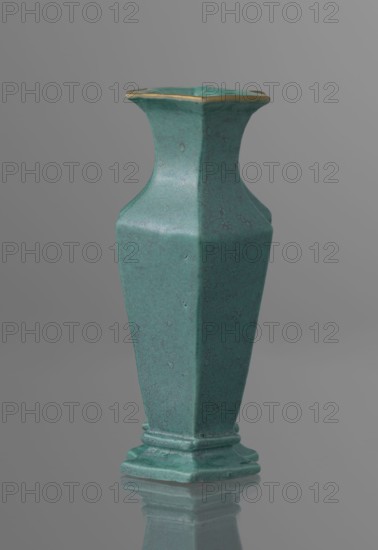 Vase, 19th century, China; Qing dynasty 1644–1911; Chinese ceramics; covered with a turquoise glaze with manganese spots; vessel; height 11.6 cm, width 4.9 cm, depth 7.1 cm, weight 0.15 kg., A single tall vase with a hexagonal form and a flared rim, standing on a stepped base and reflected on a glossy surface; the vase has a textured turquoise-green surface with subtle darker speckling and a thin metallic gold edging along the rim, set against a smooth neutral gray background.