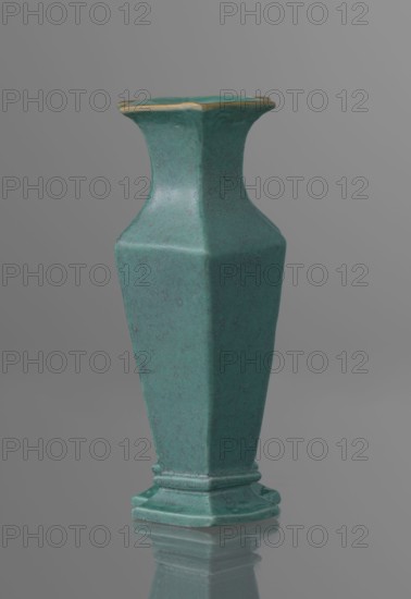 Vase, Chinese, Qing dynasty 1644–1911, 19th century. Ceramic vessel covered with a turquoise glaze with manganese spots. Height 11.6 cm; width 4.9 cm; depth 7.1 cm; weight 0.15 kg., A tall hexagonal vase with a narrow flared neck and a stepped base, shown against a plain gray background and reflected faintly on a glossy surface; the vase is a greenish teal color with subtle darker speckled mottling and a thin band of golden color along the rim.