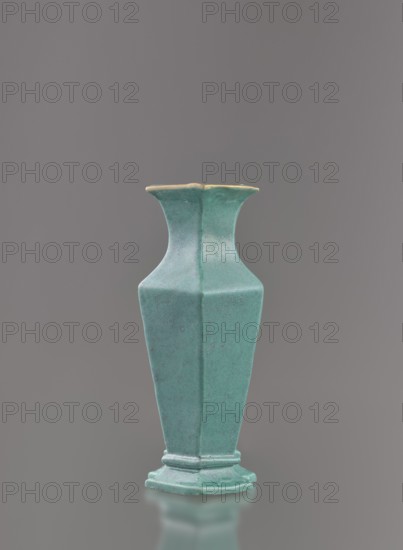 Vase, Chinese, Qing dynasty 1644–1911, 19th century. Ceramic vessel covered with a turquoise glaze with manganese spots. Height 11.6 cm; width 4.9 cm; depth 7.1 cm; weight 0.15 kg., A single tall vase with a flared rim and a hexagonal body stands centered against a neutral gray background; the vase is a muted turquoise color with subtle darker speckling and a slightly lighter rim edge, and it rests on a stepped hexagonal base that shares the same turquoise hue.
