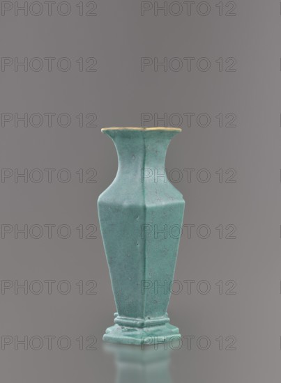 Vase, Chinese, Qing dynasty 1644–1911, 19th century. Ceramic vessel covered with a turquoise glaze with manganese spots. Height 11.6 cm; width 4.9 cm; depth 7.1 cm; weight 0.15 kg., A tall, hexagonal vase with a flared rim and stepped base sits centered against a smooth gray background; the vase has a textured turquoise-green surface with subtle darker speckling and weathered spots, and the rim shows a thin band of muted yellowish-gold along its edge.