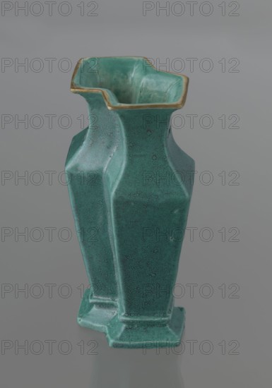 Vase, 19th century, China; Qing dynasty; Chinese ceramics. Covered with a turquoise glaze with manganese spots. Vessel with cover; height 11.6 cm, width 4.9 cm, depth 7.1 cm, weight 0.15 kg., A green ceramic vase with a textured, crackled surface and a slightly glossy finish sits against a neutral gray background; the vase has an angular, faceted form with a flared top rim that shows a thin band of yellowish-gold along its edge, an irregular square-like mouth with inward curves, a tapered body with defined vertical facets, and a stepped base, with visible variations in green tones ranging from lighter to darker areas and subtle worn spots.