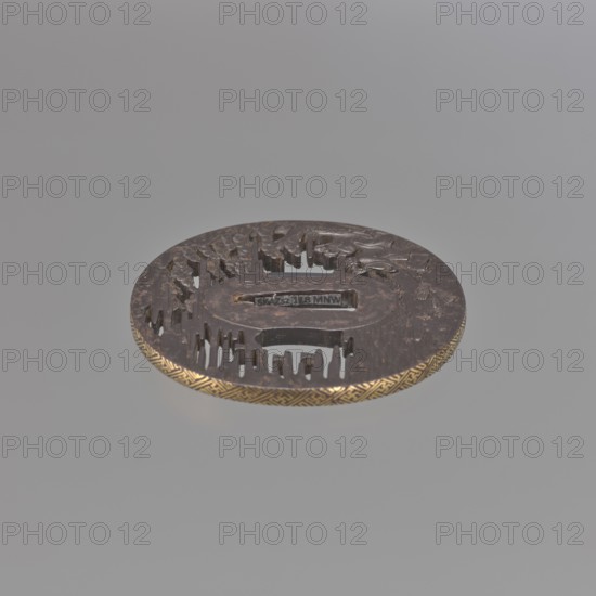 Crossguard tsuba, Takehara Tomomasa; oval tsuba tatemaru gata with rectangular edge, inlaid with gold using the nunome technique in a rinzu ornament. Side holes ryohitsu ana are part of the openwork background. Decorated with relief carving and engraving depicting two elderly people standing by the seashore beneath a spreading pine tree, gazing at the moon emerging from the fog and folding their hands in prayer; two brooms and several shells lie on the shoreline sand. The man is Jo, son of Izanagi; the woman is Uba — their legend Takasago symbolizes long life and a happy marriage. Japanese; Edo period, 18th century. Materials/subject: weapons — swords/katana crossguard tsuba; motifs: pine trees, water, moon, shells, sea waves, men's and woman's heads. Dimensions: height 7.0 cm, width 6.7 cm, depth 0.45 cm., A round metallic object with a dark brown surface and a decorative golden edge sits against a light gray background, showing carved raised and recessed patterns across its top inclu...