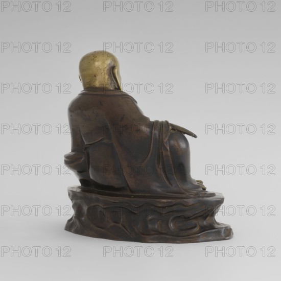 Monk Budai Laughing Buddha, Chinese art; Chinese culture; Qing 1644–1911; Buddhist art; Chinese Buddhism; Buddha of the Future, Budai iconography, Maitreya; described as a Chinese deity of Burmese origin from Shah province; 19th/20th century, China; acquisition from Burma Myanmar; sculpture; height 22.3 cm, width 23.0 cm, depth 16.0 cm, A bronze-colored sculptural figure seen from the back sitting on an irregular base with carved undulating patterns, the figure wears draped robes with visible folds and a smooth, golden-colored head; the overall palette includes brown, dark brown, bronze, and gold against a pale gray background.