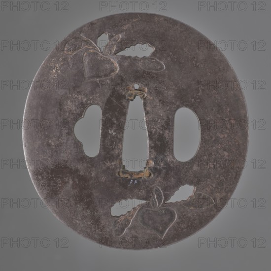 Crossguard tsuba, Masahide author, Bushû school, Japanese art, Japanese culture, Edo 1603–1868, weapons, melee weapons, swords, katana, sword crossguards, turnips, radishes, Oval tsuba tatemaru gata, rectangular edge kaku mimi. Decorated on both sides in recessed relief and partially openwork leaves with a radish motif — one of the attributes of Daikoku, the god of happiness. 18th century Edo period, Edo currently Tokyo, Japan, Asakusa, tsuba. Height 7.7 cm; width 7.3 cm; depth 0.35 cm., A round metal disc with a worn, dark brown surface and areas of lighter brown and gray patina, featuring a central vertical cutout flanked by two rounded cutouts and a smaller irregular cutout, with incised heart-shaped motifs and leaf-like shapes near the top and bottom edges, and traces of lighter metallic highlights around some cutout edges.