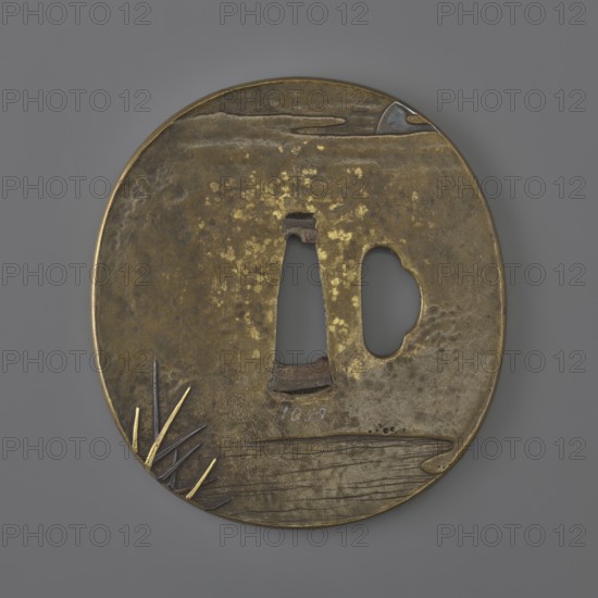 Crossguard tsuba, Tsuchiya Yasuchika 1670–1744. Oval tsuba tatemaru gata with ryohitsu ana and copper sekigane. Decorated in high relief with inlay of various metals using the iro-e takazogan technique: obverse shows a fisherman in a boat pushing with a long pole and looking at a bird flying against clouds; reverse shows reeds over water and the moon emerging from behind clouds. 1st half of the 18th century Edo period, 1603–1868, Japan Edo, now Tokyo. Materials: metal with multi-metal inlay. Dimensions: height 7.5 cm, width 6.9 cm, depth 0.4 cm., A round metal disc with a worn, uneven surface in shades of gold, brass, brown, gray, and dull silver, featuring an irregular central cutout and a nearby rounded void, with textured areas of brighter gold speckling and darker tarnished patches, a few thin angular protrusions at the lower left in muted gold and dark gray, subtle engraved lines and grooves near the bottom suggesting layered texture, and a small curved inlay of bluish-silver near...