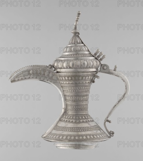 Teapot, Persian, Qajar dynasty 1785–1925. Teapot/kettle for beverages coffee/tea, ceramic metal vessel with geometric motifs. 19th–20th century, Iran. Height 24 cm; width 21.5 cm; diameter 12.5 cm; weight 580 g., A metal vessel with an elongated curved spout and a high domed lid topped by a finial, featuring a sweeping handle opposite the spout; the surface is covered in repeating raised geometric and leaflike patterns and bands of textured decoration giving a ribbed appearance; the form narrows at the midsection and flares at the base into a conical foot; visible colors are silver and shades of gray against a neutral light-gray background.