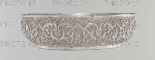 Bowl, Islamic art, Turkish culture, Ottoman dynasty 1299–1922, geometric motifs, plant ornament, tugra of Abdulhamid II Ottoman sultan; 1842–1918, 1876–1909, Turkey, silver hammam vessel, height 5.6 cm, diameter 19.0 cm, A shallow, ornate metal bowl with a polished surface sits against a plain light gray background; the bowl displays an all-over raised floral and foliate relief pattern around its exterior with curving vines and stylized leaves and blossoms, a decorative border along the rim, and a slightly rounded base. The visible colors are shades of silver and gray.