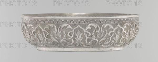 Bowl, maker, purchase, Islamic art; Turkish, Ottoman dynasty 1299–1922. Silver hammam bowl with geometric motifs, plant ornament, and tugra of Abdulhamid II Ottoman sultan; 1842–1918. Dated 1876–1909. Vessel, height 5.6 cm, diameter 19.0 cm., A shallow, round metal bowl with ornate raised floral and foliate scrollwork covering its exterior, showing a repeating pattern of stylized leaves and blossoms within arch-like cartouches, a narrow beaded rim and a plain rounded foot; the visible colors are silvery gray tones with areas of darker gray patination and lighter reflective highlights.
