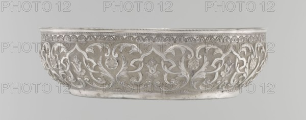 Bowl, Islamic art, Turkish culture, Ottoman dynasty 1299–1922, geometric motifs, plant ornament, tugra of Abdulhamid II Ottoman sultan; 1842–1918, 1876–1909, Turkey, silver hammam bowl, vessel, height 5.6 cm, diameter 19.0 cm, A shallow ornate bowl with raised scrolling floral and foliate motifs around its exterior, featuring curving leaf shapes and stylized blossoms in relief, a decorative patterned band near the rim, and a smooth flat base; the visible colors are silver, light gray, and pale metallic tones.