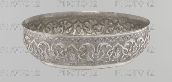 Bowl, purchased; Islamic art, Turkish, Ottoman dynasty 1299–1922; geometric motifs and plant ornament; tughra of Abdulhamid II Ottoman sultan; 1842–1918; dated 1876–1909; silver hammam bowl; Turkey; vessel; height 5.6 cm, diameter 19.0 cm, A shallow round metal bowl with ornate raised floral and scrolling patterns covering its exterior and interior, rendered in metallic silver tones with areas of darker gray patina and lighter reflective highlights; the rim has a band of small repeating decorative elements, and the interior shows similar embossed motifs creating a textured surface; the background is a uniform pale gray.