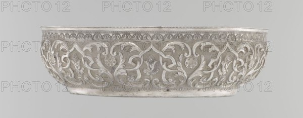 Bowl, Islamic art, Turkish, Ottoman dynasty 1299–1922, geometric motifs, plant ornament, tughra of Abdulhamid II Ottoman sultan; 1842–1918, 1876–1909, Turkey, silver hammam bowl, vessel, height 5.6 cm, diameter 19.0 cm, A shallow, round metal bowl with ornate raised floral and foliate relief covering its exterior, showing intricate scrolling leaves and stylized flowers in a repeating pattern; the rim has a decorative band with a smaller repeating motif and a slightly scalloped edge; the bowl rests on a narrow base rim and the surface shows subtle variations in sheen and texture; the visible colors are silver, gray, and white.