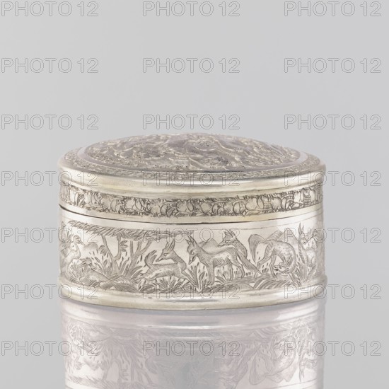 Box with lid; creator, 19th century India; Indian art; materials: tin/container vessel; dimensions: height 3.5 cm, diameter 6.5 cm, weight 105 g. Decoration: animals—lions, antelopes, jackals, cranes—trees, plant and geometric ornaments; applied decoration. Function: box/vessel., The image shows a small oval metal box with an engraved lid and sides, the metal appearing silver and pale gray with darker etched lines; the lid has ornate raised and incised decorative patterns, the rim and banding around the top and bottom are smooth and rounded, and the side surface features an engraved scene of animal figures and vegetation rendered in fine line work; the box rests on a reflective pale surface that mirrors its underside, and the background is a uniform light gray.