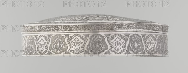 Lidded box, Persian, Qajar dynasty 1785–1925; 19th/20th century; Iran, Isfahan. Geometric and floral motifs plant ornament. Vessel; height 3.0 cm, diameter 13.0 cm; weight 285 g., A shallow, oval-shaped metallic object with intricate engraved patterns seen from the side, showing a decorative band around its rim featuring a repeated series of ornate medallion motifs and a narrower floral frieze above; the metal appears silvery with darker engraved areas creating contrast, and the background is a light gray.