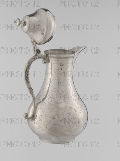 Teapot with a lid; maker, 19th century; Ottoman dynasty 1299–1922; Turkish; vessel for beverages teapot; materials/technique not specified; geometric motifs and plant ornament; height 20.3 cm; diameter 9.7 cm; weight 300 g., A metallic pitcher with a hinged domed lid is shown against a plain light gray background; the pitcher and lid are silver in color with a slightly reflective surface and visible engraved floral and geometric patterns; the handle is ornate with curved scrollwork and some darker tarnished areas, and the spout is slender and slightly upturned; the overall shape is bulbous at the base, narrowing at the neck, with a decorative band around the rim; the image shows a few small spots of discoloration and subtle surface scratches on the metal.
