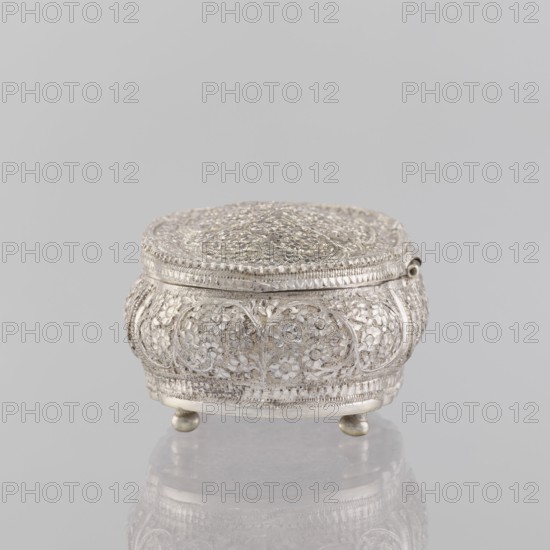 Box with lid; maker, purchase provenance; Indian art; Indian; plant ornament; 19th–20th century; India; varia; height 4.5 cm; width 12.5 cm; depth 6.5 cm; weight 151 g, A small ornate round box with a domed lid and three small rounded feet, covered all over in detailed raised floral and foliate patterns and textured banding; the object appears metallic with a silver color and shows highlights and subtle darker silver shadows.