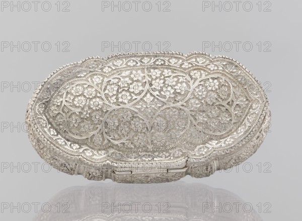 Box with lid; maker, plant ornament; Indian; 19th–20th century; India; dimensions: height 4.5 cm, width 12.5 cm, depth 6.5 cm; weight 151 g., An oval ornate metal dish with an openwork floral pattern covering its surface, showing a repeating motif of flowers and intertwining vines; the rim is scalloped with decorative edging and the sides continue the intricate pierced design, all rendered in a reflective silver tone against a pale gray background with a faint mirrored reflection of the object below.