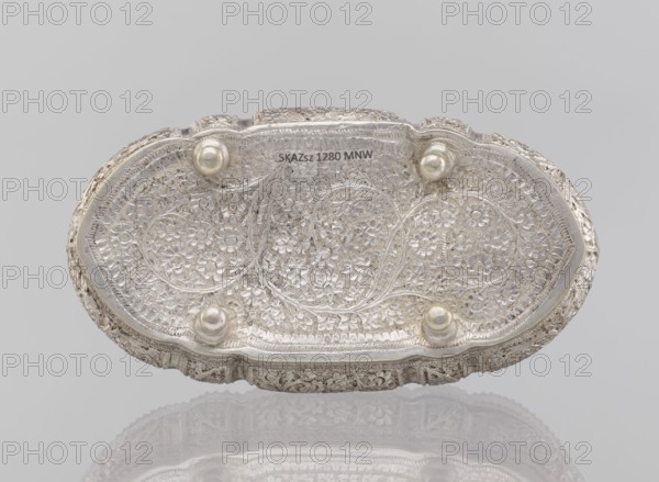 Box with lid, plant ornament, 19th/20th century, India, height 4.5 cm, width 12.5 cm, depth 6.5 cm, weight 151 g, An oval decorative object with an embossed floral pattern across its surface, showing a group of raised rounded feet and a scalloped edge; the visible colors are silver, pale gray, off-white, and a hint of reflective sheen.