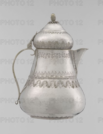 Teapot, 19th century, Turkish Ottoman dynasty, 1299–1922. Silver vessel teapot, height 17.0 cm, diameter 10.9 cm, weight 320 g. Decoration: geometric motifs, plant ornament lambrequin, zigzag. Function: teapot/jug. Culture: Islamic art., A metallic pitcher with a rounded, bulbous lower body tapering to a narrower midsection and topped by a domed lid with a small finial, shown against a plain light background; the pitcher displays decorative etched patterns around the neck, midsection, and near the base, with a curved spout on one side and a slender handle attached on the opposite side; visible colors include silver tones of the metal and subtle variations of gray.