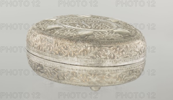 Box with lid, Islamic art, Turkish, Ottoman dynasty 1299–1922, plant motifs, geometric motifs, 19th century, Turkey, varia; height 9.0 cm, width 19.5 cm, depth 15.7 cm, weight 210 g, A rounded decorative box resting on small rounded feet, with an embossed surface covered in ornate swirling leaf and vine patterns and raised rounded embellishments on the lid; the object appears metallic with a silvery tone and areas of warm pale gold and beige patina, set against a pale neutral background in shades of light gray and off-white.