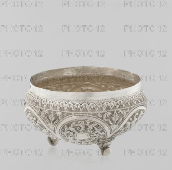 Vessel with a lid, Islamic art, Turkish, Ottoman dynasty 1299–1922, plant ornament with flowers and plant tendril, marked coat of arms, 19th century, Turkey, vessel, weight 240 g, height 11.7 cm, diameter 10.5 cm, A decorative bowl with ornate embossed patterns sits against a plain light gray background; the bowl is metallic with a silver color and shows textured floral and circular motifs around its rounded body, a smooth silver rim, and a slightly darker interior with visible decorative detailing; the bowl rests on a few small rounded feet and the overall tones in the image are shades of silver, gray, and off-white.