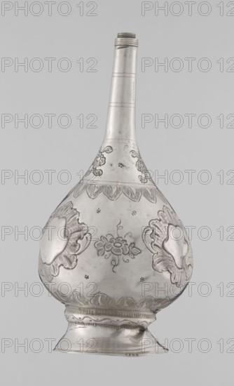 Bottle for spraying water soaked in perfumes, Islamic art; vessel with plant and floral ornament; decoration: multi-leafed undecorated cartouches alternating with small flowers. 19th–20th century; possibly Turkey or North Africa. Weight 113 g; height 17.5 cm; diameter 8.0 cm., A tall, teardrop-shaped metal vessel with a long narrow neck and a rounded body, shown against a plain light gray background; the surface of the vessel is metallic silver with darker etched or engraved floral and leaf motifs decorating the bulbous section and a scalloped band near the shoulder; there are raised ornamental medallion-like shapes on the sides and a central floral cluster on the front; the neck has a few subtle horizontal bands and a threaded rim at the top; the foot is flared with layered decorative ridges and a slight dent on one side; overall tones visible are silver, light gray, and subtle darker gray in the engraved details.
