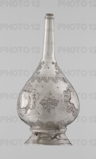 Bottle for spraying water soaked in perfumes; maker, Islamic art; vessels; plant ornament and floral motifs; decoration: multi-leafed undecorated cartouches alternating with small flowers; 19th/20th century; origin possibly Turkey or North Africa; vessel; weight 113 g; height 17.5 cm; diameter 8.0 cm., A single metal vessel with a long narrow neck and a bulbous body stands against a plain light gray background; the vessel appears silvery-gray with darker engraved or etched decorative motifs including floral shapes, scalloped bands, and ornate medallion-like designs around the rounded body, and the base flares outward with embossed ridges and patterned borders.