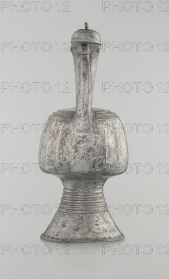 Jug aftabe, unknown provenance; Islamic art; 19th century; North Caucasus; jug aftabe for water; vessel; height 30.0 cm, length 14.8 cm, diameter 12.0 cm., A single weathered metal vessel with a tall narrow neck and a bulbous body set on a flared pedestal base, showing a rough, pitted surface texture and areas of worn finish; the form has subtle linear ridges around the shoulder and neck, a rounded lid with a small protrusion on top, and small rounded projections near the lid, all rendered in shades of gray with hints of muted brown and pale metallic highlights against a pale gray background.