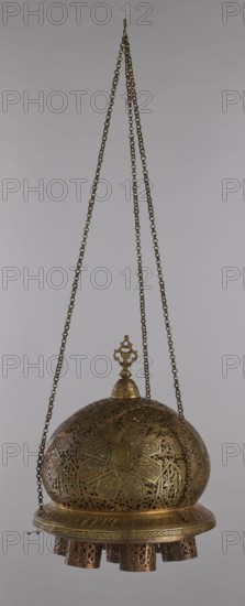 Lamp, Islamic art, Arabic culture, metals, lighting, geometric ornament, Arabic inscriptions. Cover decorated with a star motif. Disc base with seven holes for glass sleeves glass oil containers missing. 19th/20th century, Damascus, Syria. Lamp; height 40 cm, diameter 32 cm, weight 2.4 kg., A hanging ornate metal lantern suspended by a few long chains against a plain light gray background, the lantern dome and base displaying an intricate pierced geometric and floral pattern with filigree work, the metal showing a mix of brass and bronze tones and a slightly aged patina, a decorative finial on top with a small loop where the chains meet, and a ring of cylindrical perforated extensions dangling from the lower rim, all elements rendered in metallic gold, brass, and brown hues.