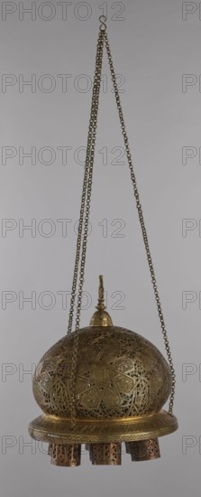 Lamp, Islamic art, Arabic culture, metals, lighting; geometric ornament, Arabic inscriptions. Cover decorated with a star motif. Disc base with seven holes for glass sleeves glass oil containers missing. 19th–20th century, Damascus, Syria. Lamp; height 40 cm, diameter 32 cm, weight 2.4 kg., A hanging ornate metal object suspended by a group of chains, with a domed, perforated upper section decorated with intricate geometric and floral patterns and a small finial on top; the metal surface shows a golden color with darker bronze accents, and a round flat rim beneath the dome features engraved patterns; below the rim hang several short cylindrical elements with openwork designs in darker bronze tones against the golden body, all set against a plain light gray background.