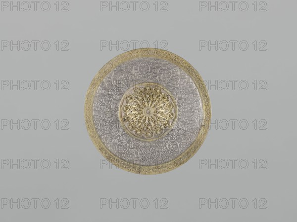 Mirror frame, scrap - purchase; Islamic art; mirror frame with plant motifs and geometric ornament including 6-pointed star Solomon's Seal; stylized plant patterns in a geometric arrangement; 19th century; Turkey, / Iran ; weight 685 g; diameter 25.5 cm; height 1.2 cm., A circular decorative object centered on a plain background, featuring a metallic appearance with a gold outer rim and an ornate gold patterned central medallion, surrounded by a silver-toned area embossed with intricate floral and vine motifs; the colors visible include gold, silver, and shades of gray, with the background appearing light gray.