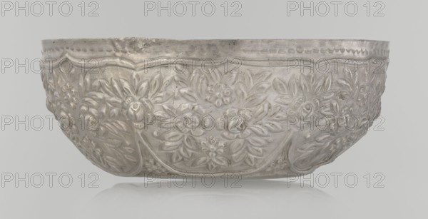 Bowl, late 19th century, Turkey; Ottoman dynasty 1299–1922; Islamic art; vessel; decorated with floral and plant ornament—wall decorated with floral motifs in the valance; weight 295 g; height 7.0 cm; diameter 18.0 cm., A shallow decorative bowl with an embossed floral pattern covers its exterior, showing a repeating design of stylized flowers and leaves in low relief; the surface appears metallic with a silvery-gray color and subtle darker areas from tarnish or wear, and the rim has a scalloped border detail.