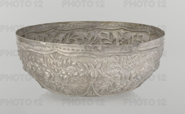 Bowl, late 19th century, Turkey; Ottoman dynasty 1299–1922; Islamic art, Turkish; vessel, height 7.0 cm, diameter 18.0 cm, weight 295 g; decorated with floral and plant motifs, wall decorated with floral motifs in the valance., A shallow, round metal bowl with an embossed floral pattern covering its exterior and interior, showing raised flowers and leaves in a repeating decorative motif; the rim has a scalloped embossed border and the bowl sits on a reflective surface. The visible colors are silver, gray, and hints of off-white.