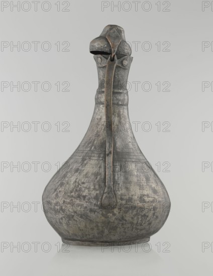 Jug aftabe, Islamic art, Islamic culture, jugs, water, geometric ornament, 19th century, Caucasus, Central Asia, vessel, height 31.5 cm, width 20.5 cm, diameter 18 cm, A single metal vessel with a bulbous base tapering to a narrow neck and topped by a rounded lid with a hinged strap; the surface shows a weathered, mottled patina in shades of gray, dark gray, and hints of brownish tones, with areas of lighter gray and off-white wear; a long vertical handle or strap runs from the lid down the neck and body, appearing darker at the edges with subtle brown highlights; the object sits on a shallow rounded foot against a plain light gray background.