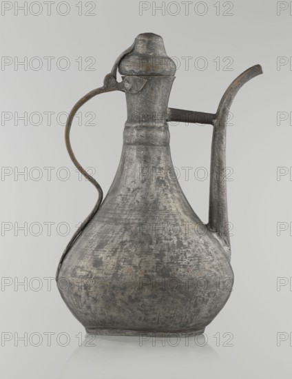 Jug aftabe, Islamic art, Islamic culture, 19th century, Caucasus, Central Asia, jugs, water, geometric ornament, vessel; height 31.5 cm, width 20.5 cm, diameter 18 cm., An aged metal ewer with a bulbous body tapering to a narrow neck, showing a textured, weathered surface in shades of gray with areas of darker and lighter gray and hints of brownish discoloration; it has a curved spout extending upward from the neck and a sinuous handle attached from neck to shoulder with a small hinged lid at the top, all matching the same gray and brownish tones, and the object rests on a subtle rounded base against a pale gray background.
