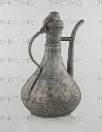 Jug aftabe, Islamic art, Islamic culture, jugs, water, geometric ornament, 19th century, Caucasus, Central Asia, vessel; height 31.5 cm, width 20.5 cm, diameter 18 cm, A metal pitcher with a bulbous body, narrow neck, and hinged lid sits against a light background; it has a curved handle attached near the neck and a long, slightly curved spout on the opposite side, showing a weathered, textured surface with visible wear and patina in shades of gray, silver, dark gray, and hints of brown.