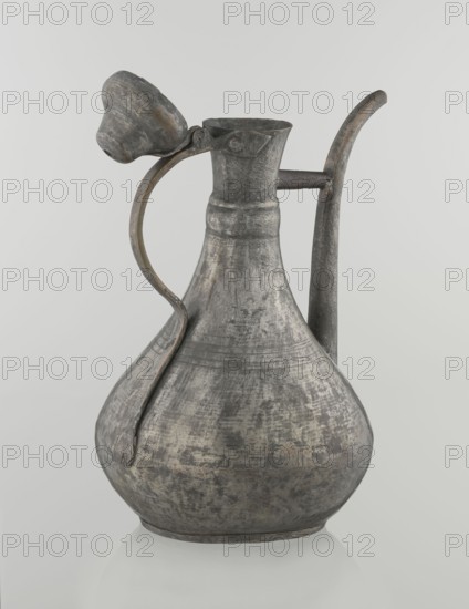 Jug aftabe, Islamic art, Islamic culture, jug for water, geometric ornament, 19th century, Caucasus, or Central Asia, vessel; height 31.5 cm, width 20.5 cm, diameter 18 cm, A metal pitcher with a bulbous body and a narrow neck, shown against a plain light gray background, displaying a weathered surface in shades of gray with areas of darker gray and subtle brownish and greenish patina; it has a curved handle attached from neck to shoulder and a long spout rising from the back, and a small ladle-like cup rests near the top connected by a short metal arm, all showing textured, worn metal with faint banded ridges around the upper body.